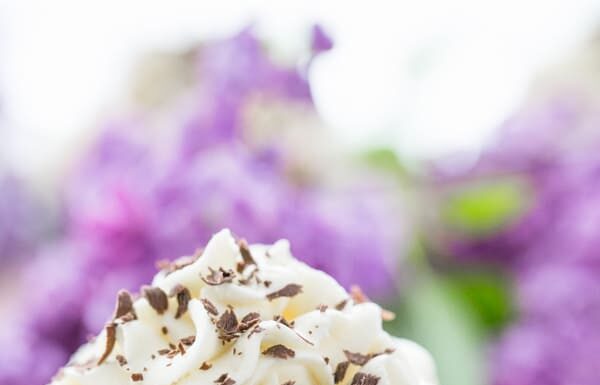A close up of a dark chocolate cupcake with white chocolate frosting with flowers behind it 