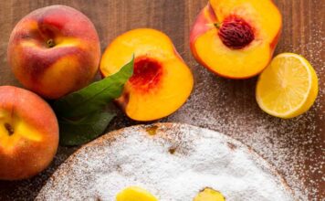 Fresh peach cake with one slice to serve. Decorated with powdered sugar and fresh peach slices