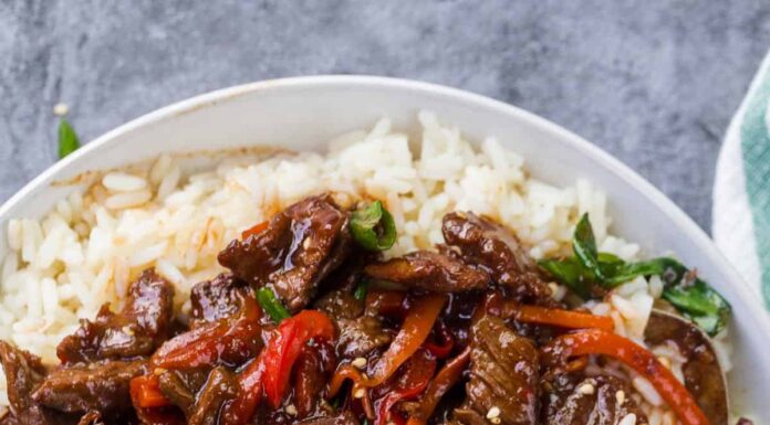Mongolian Beef and vegetables over a bed of rice with a spoon and a napkin.