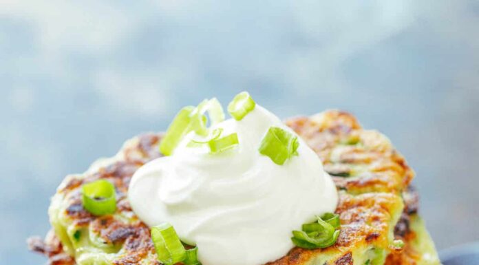 Stack of zucchini fritters topped with sour cream and scallions